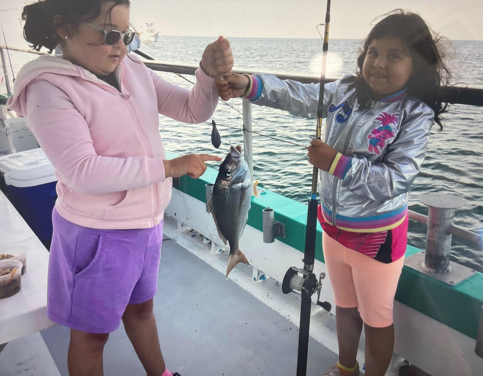 a little girl standing next to a woman holding a fish