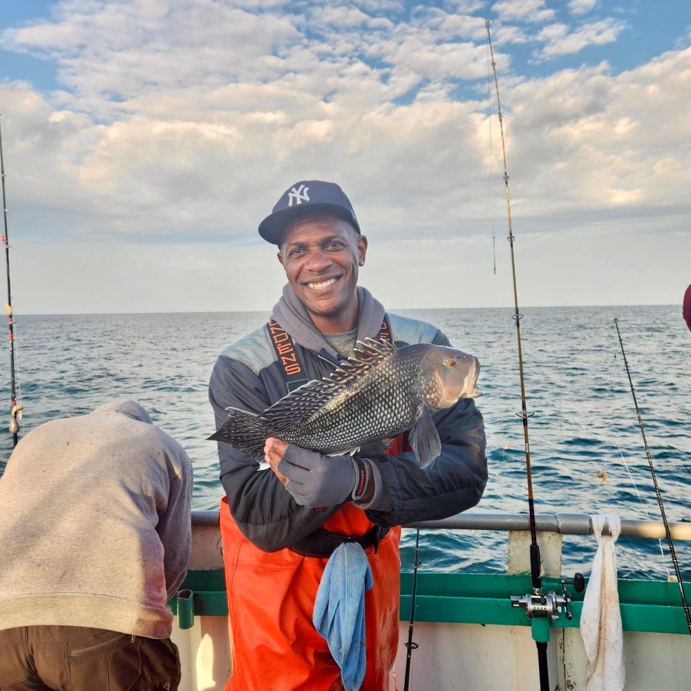 Jerry Kenney holding a fish on a boat in a body of water