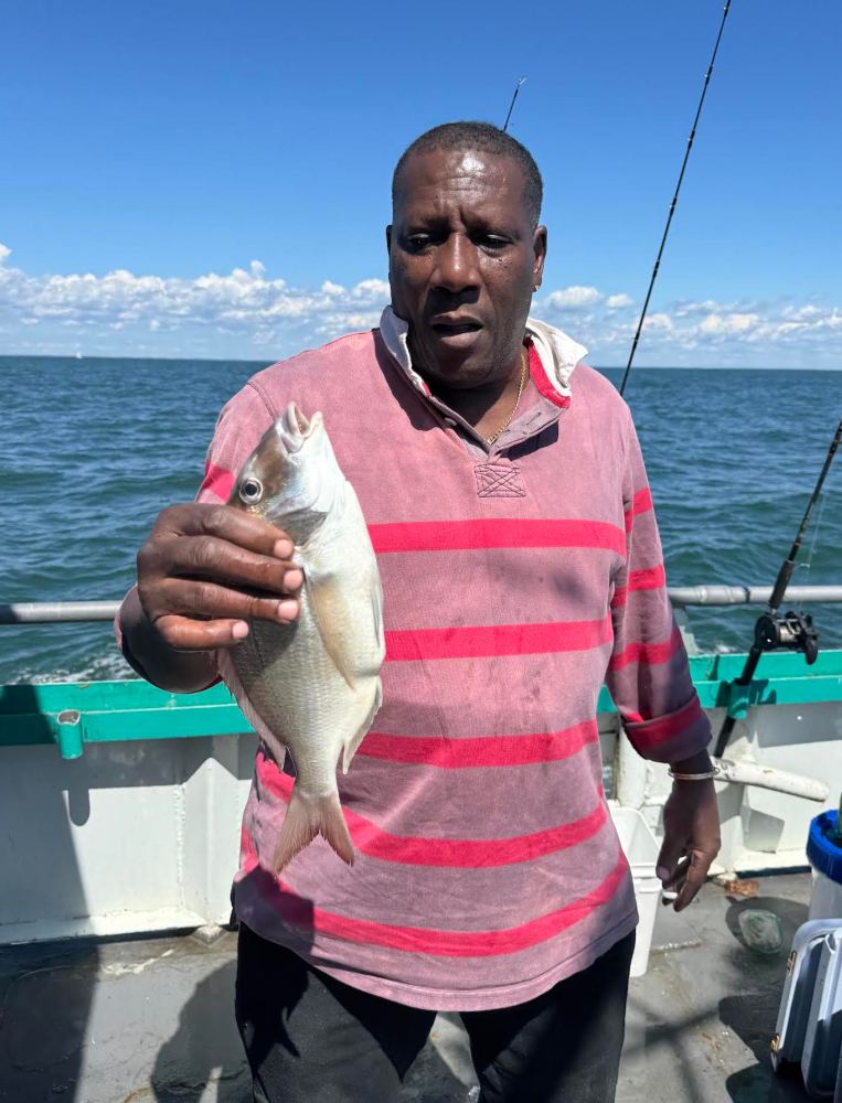 Man holding a fish on a boat with the ocean in the background.