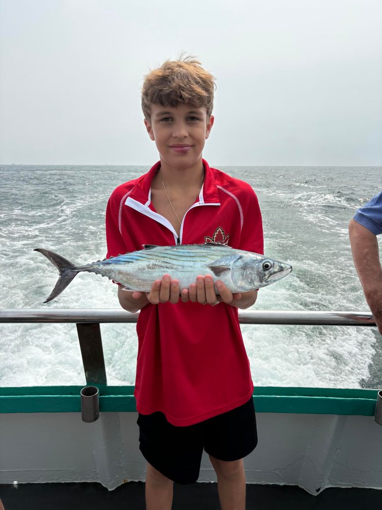 Boy in red shirt holding a large fish on a boat with ocean in background.