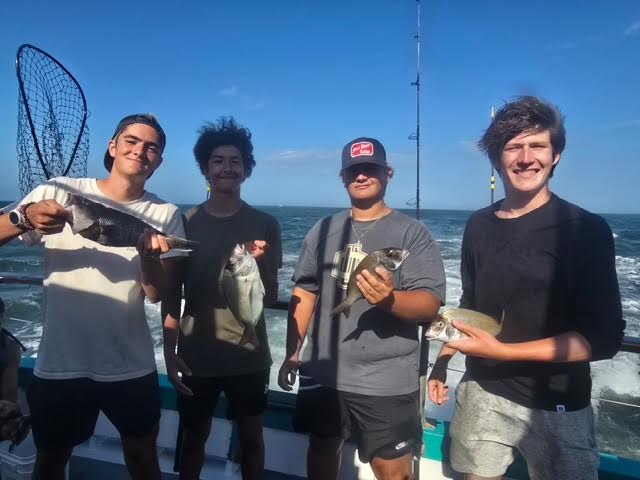 Four people on a boat holding fish, with ocean waves in the background.
