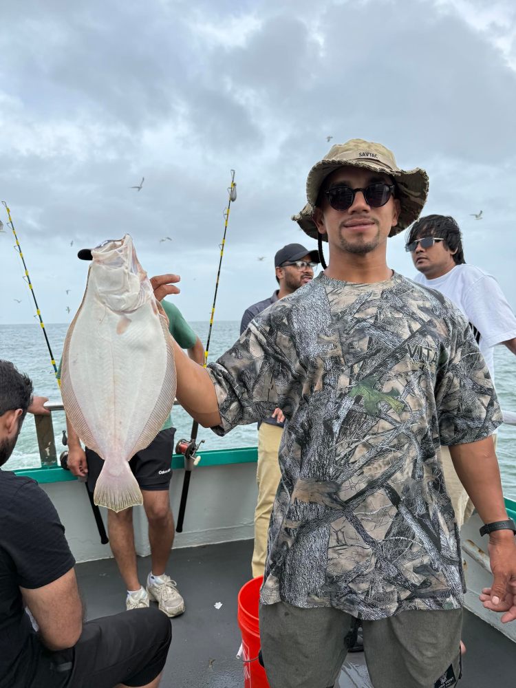 Person in camo shirt holding a fish on a boat with ocean and cloudy sky in background.