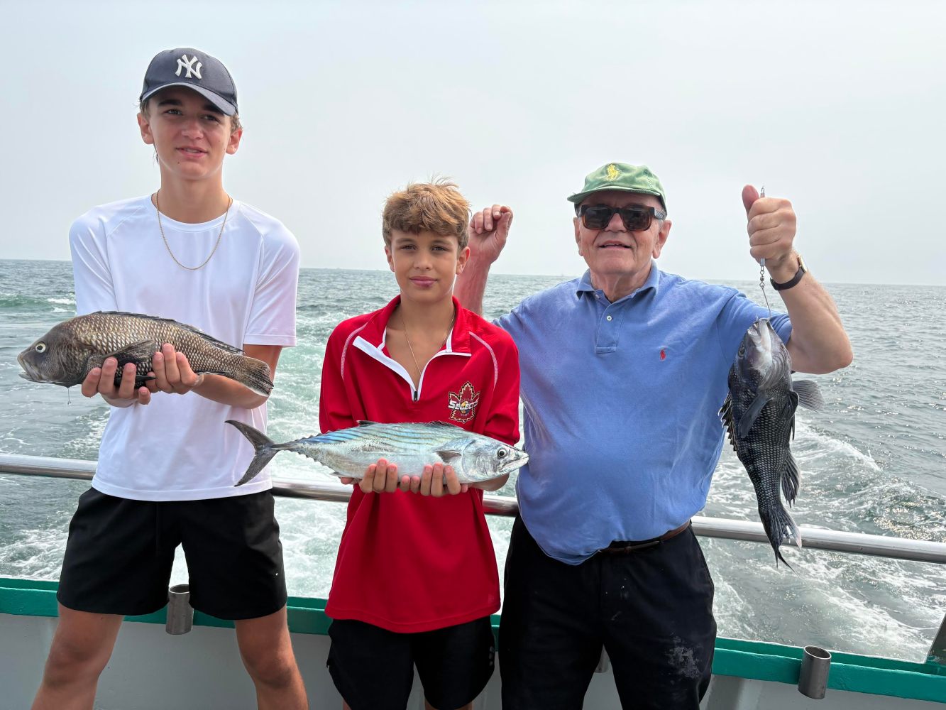 Three people on a boat holding fish with the ocean in the background.