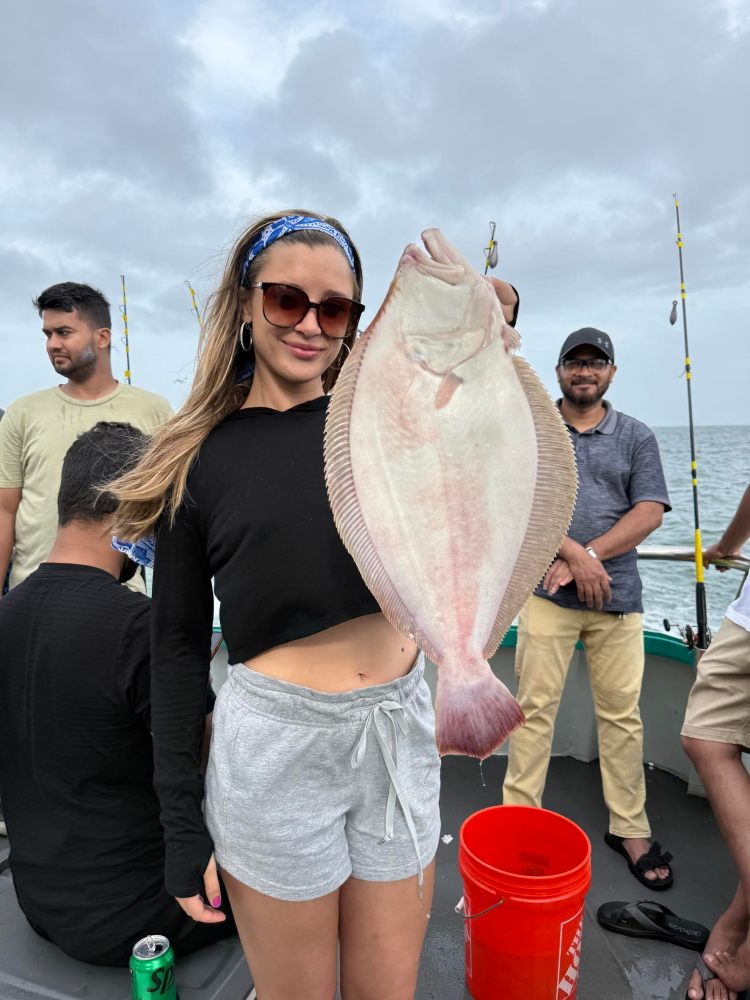 Person on boat holding a large fish, with others in the background and a cloudy sky.