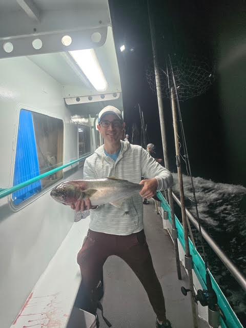 Person holding a large fish on a boat at night.