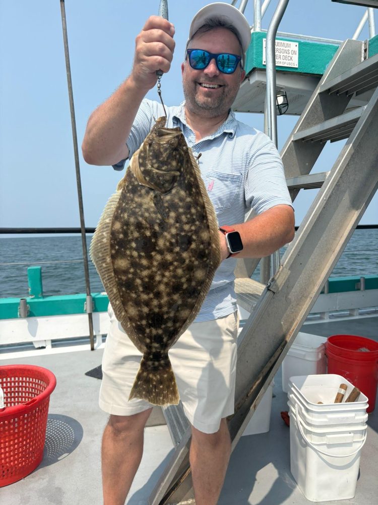 Person smiling and holding a large fish on a boat deck next to stairs.