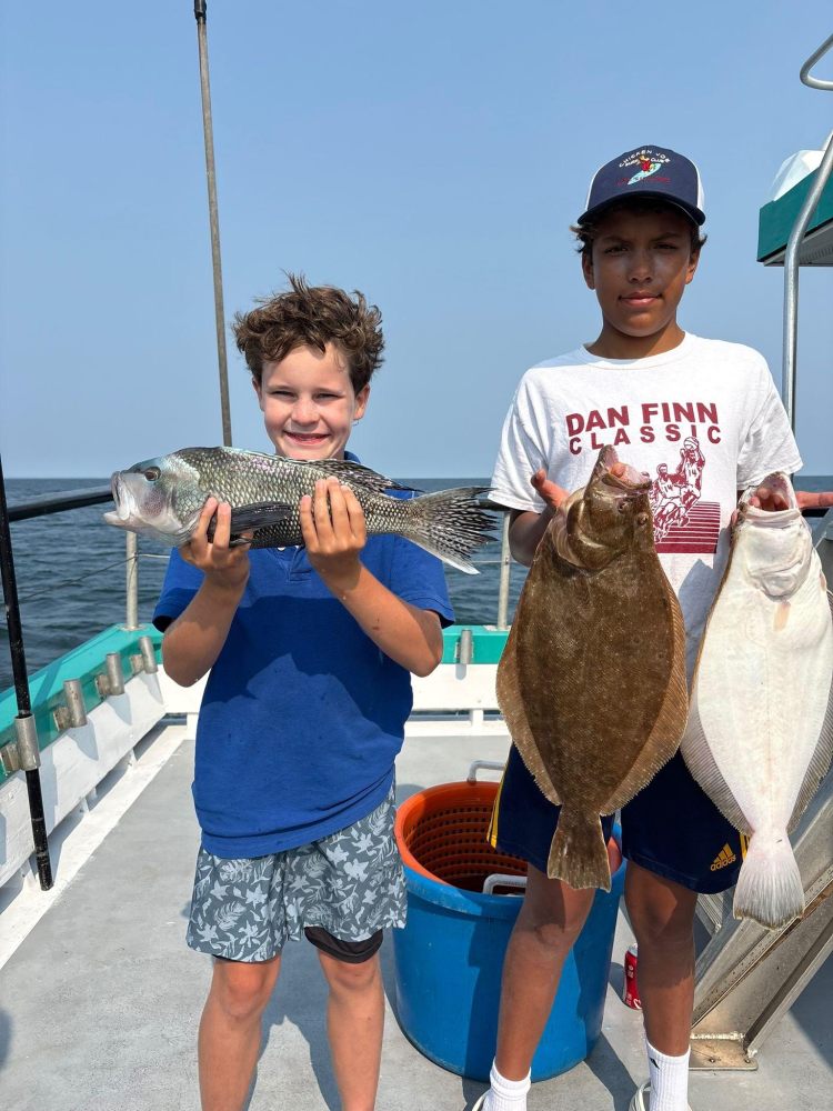 Two boys on a boat holding freshly caught fish, blue sea in the background.
