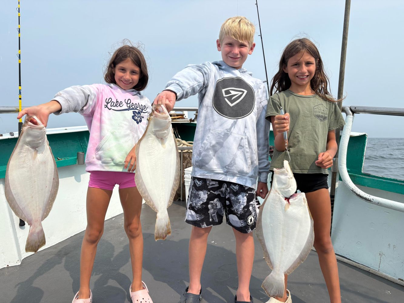 Three children on a boat each holding a flatfish they caught.
