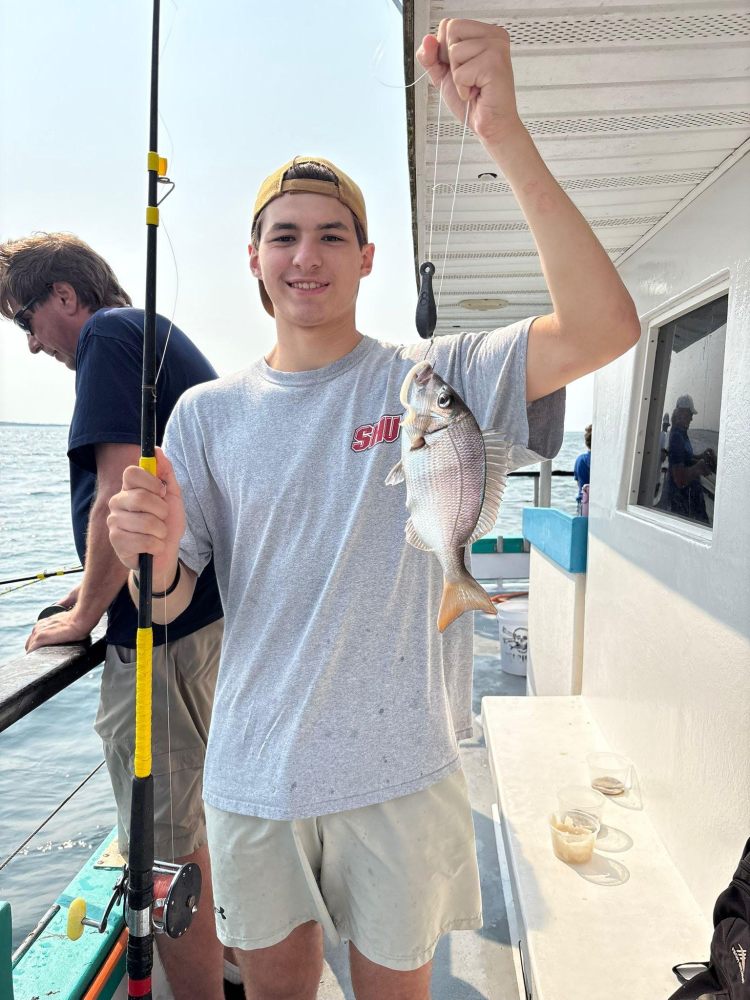Person holding a fishing rod and a fish on a boat, smiling at the camera.
