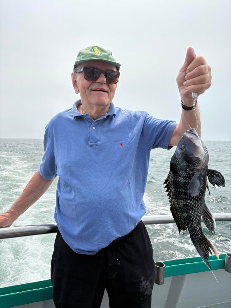 Man in sunglasses and hat holding a fish on a boat at sea.