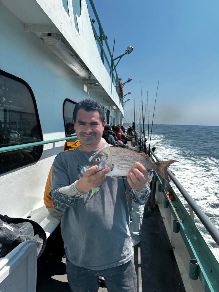 Man holding a fish on a boat with fishing rods and ocean background.