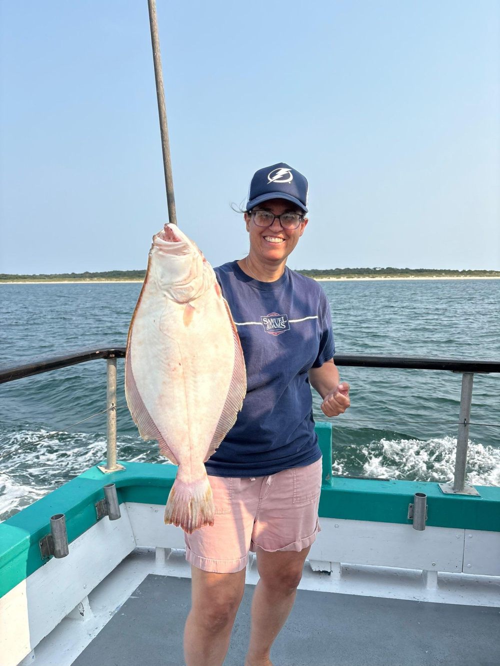 Person holding a large flounder on a boat in sunny weather.