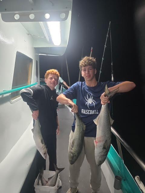Two people on a boat holding large fish at night.