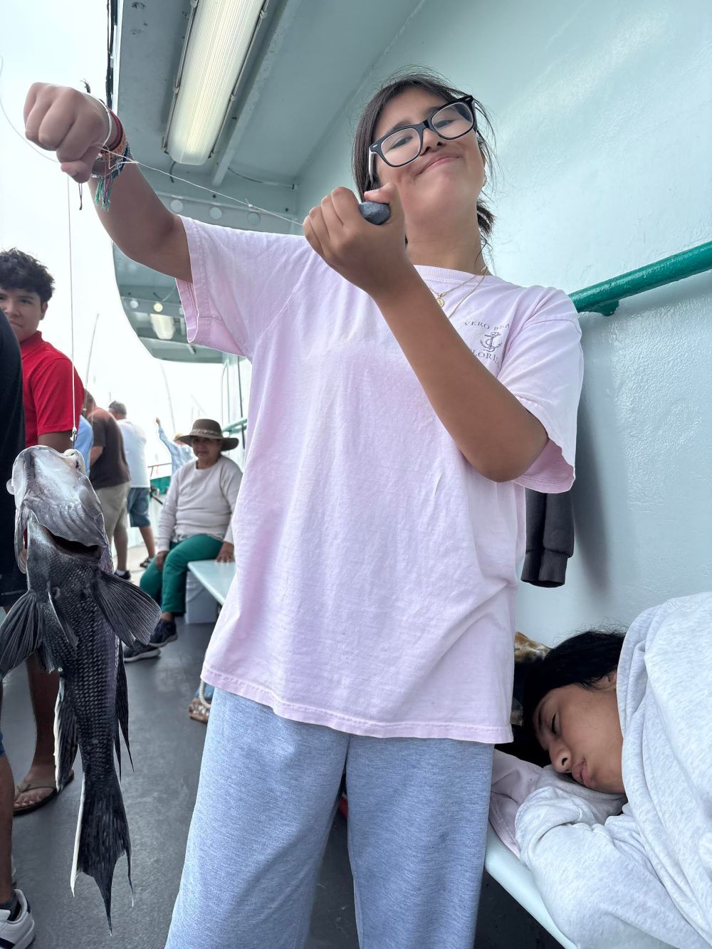 Person holding a fish with a sleepy passenger beside on a boat.