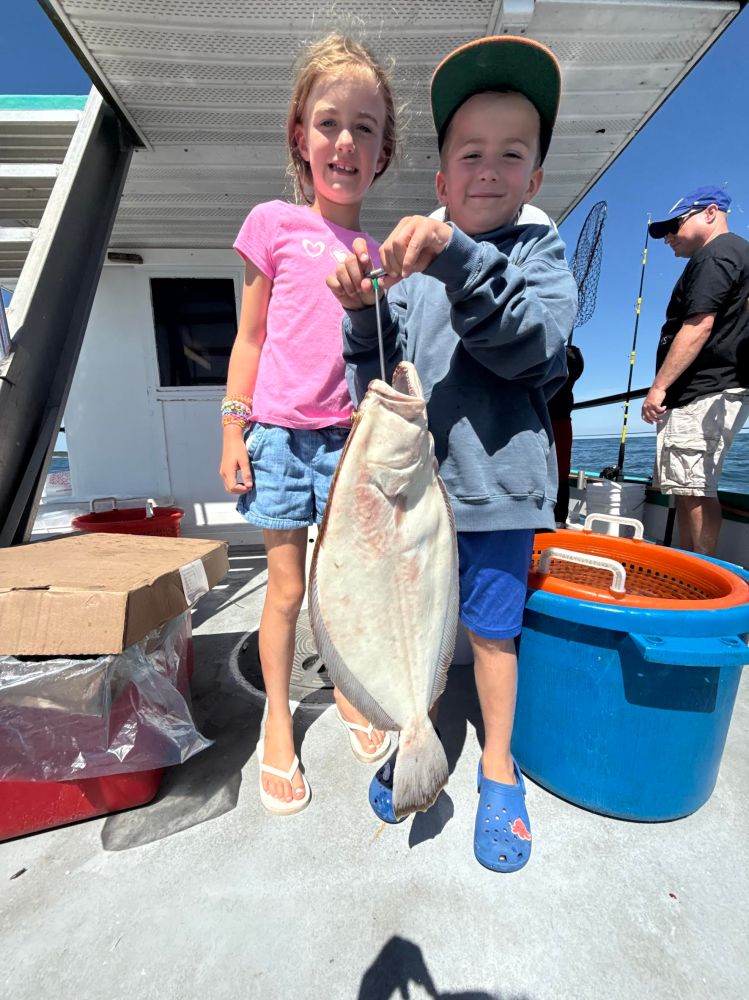 Two kids happily holding a large fish on a boat, with fishing gear in the background.
