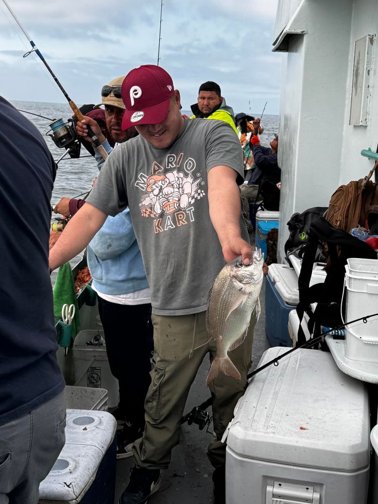 Man on a boat holding a fish, surrounded by fishing gear and other people.