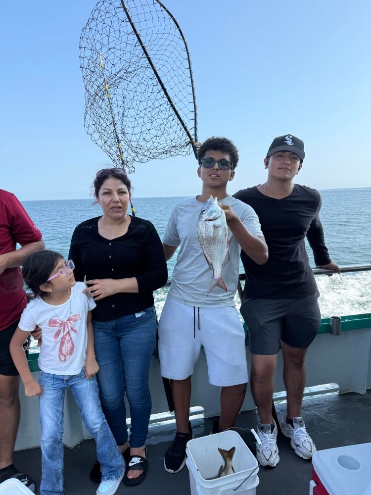 Group of four people on a boat, one holding a fish, with the ocean in the background.