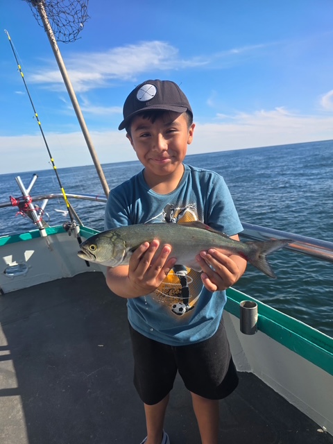 Young boy on a boat holding a fish with the ocean in the background.