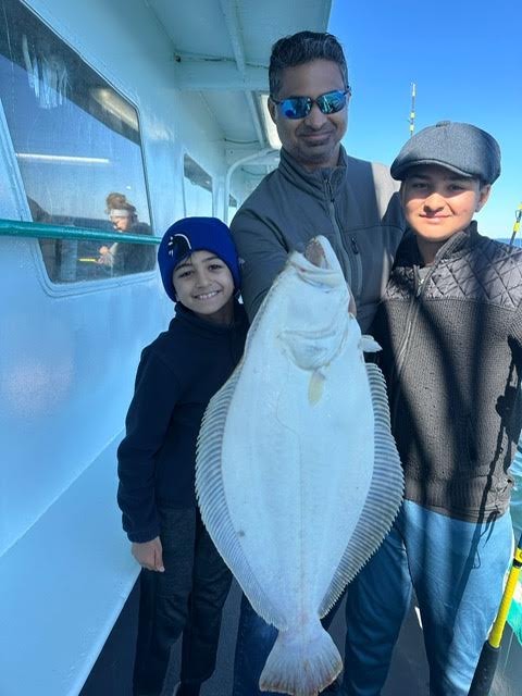 Three people smiling on a boat holding a large flat fish.