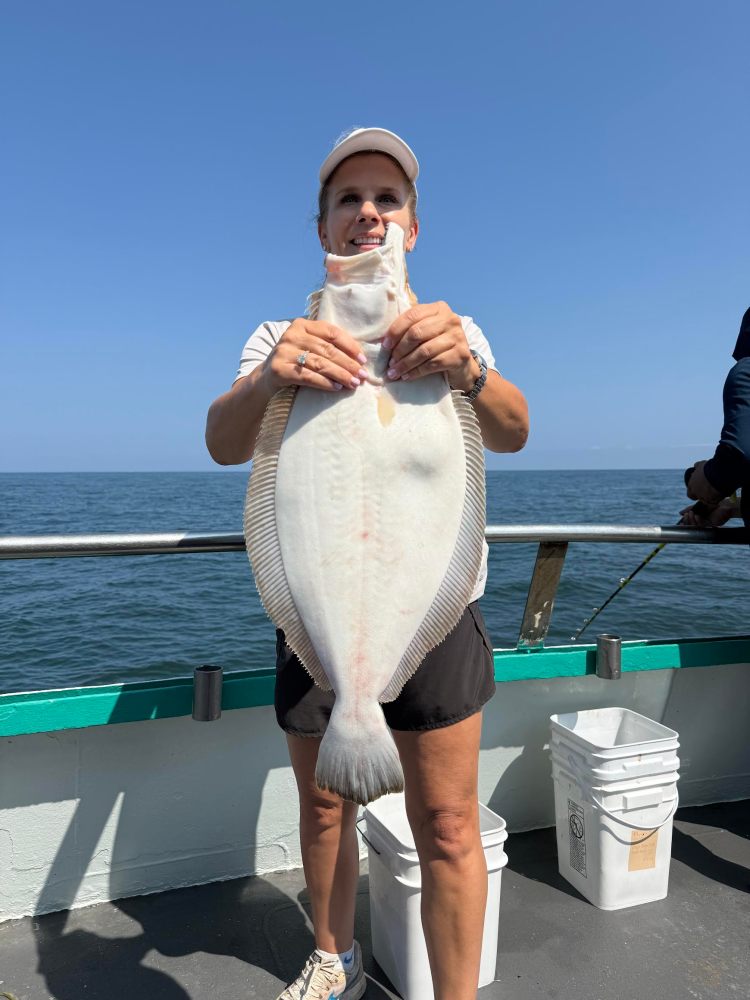 Person holding a large flat fish on a boat with ocean in the background.
