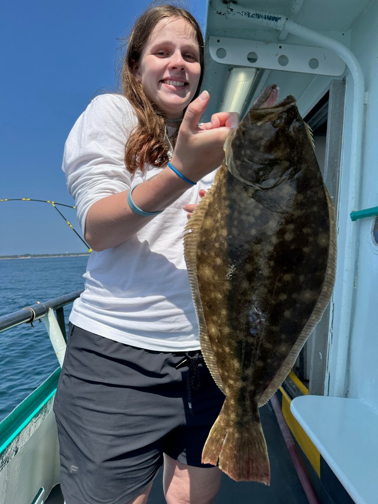 Person on a boat smiling and holding a large fish under a clear blue sky.
