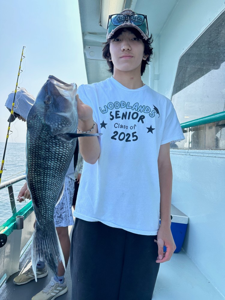 Person in a cap holding a fish on a boat, wearing a 'Woodlands Senior Class of 2025' shirt.