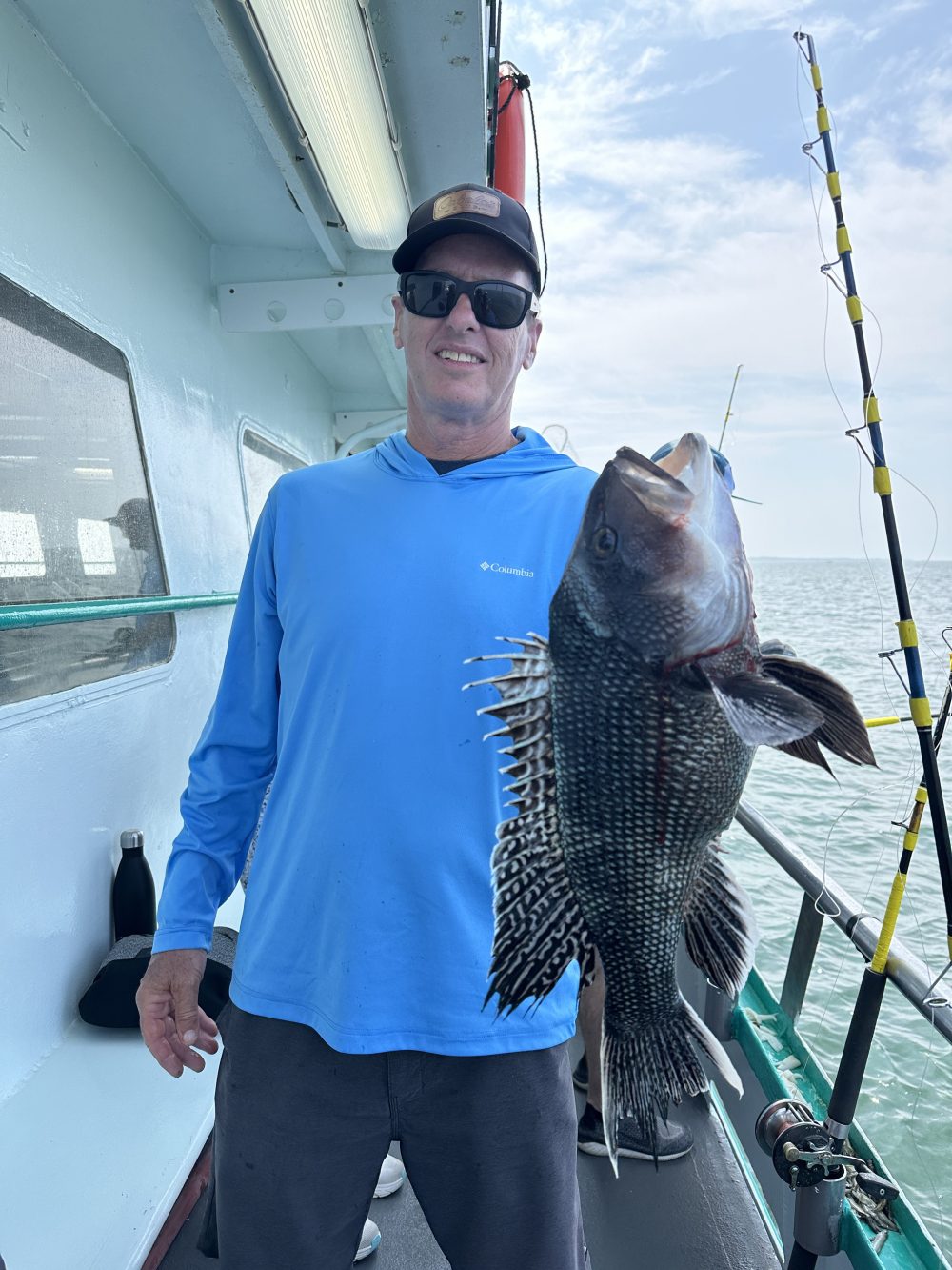 Person on a boat holding a large fish with fishing rods in the background.