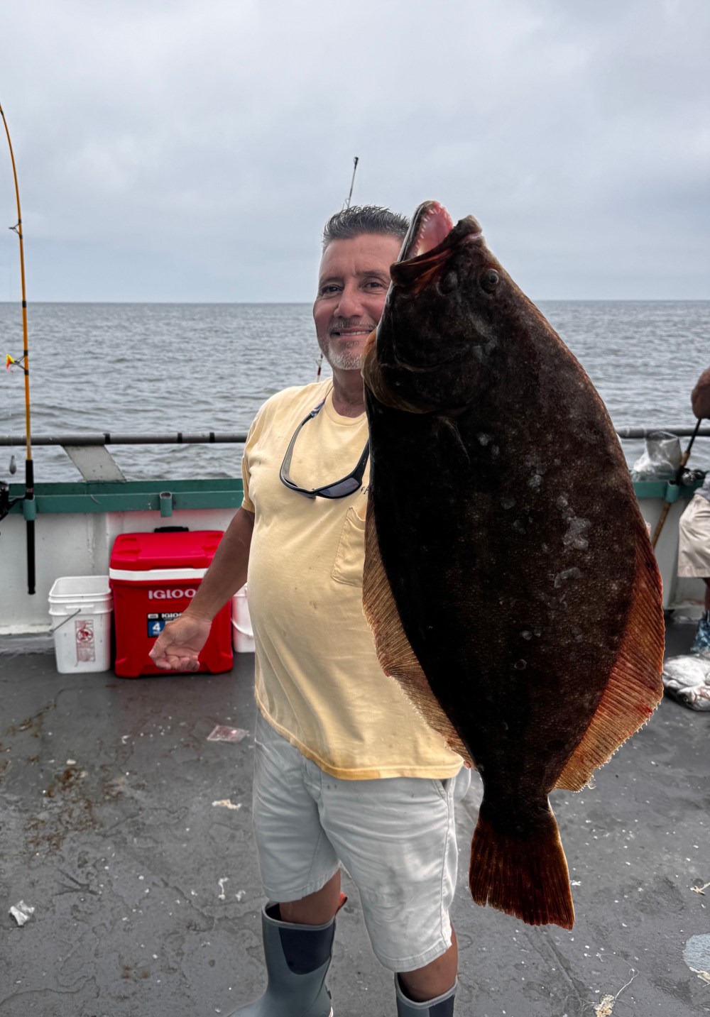 Person holding large flatfish on a boat with ocean background.
