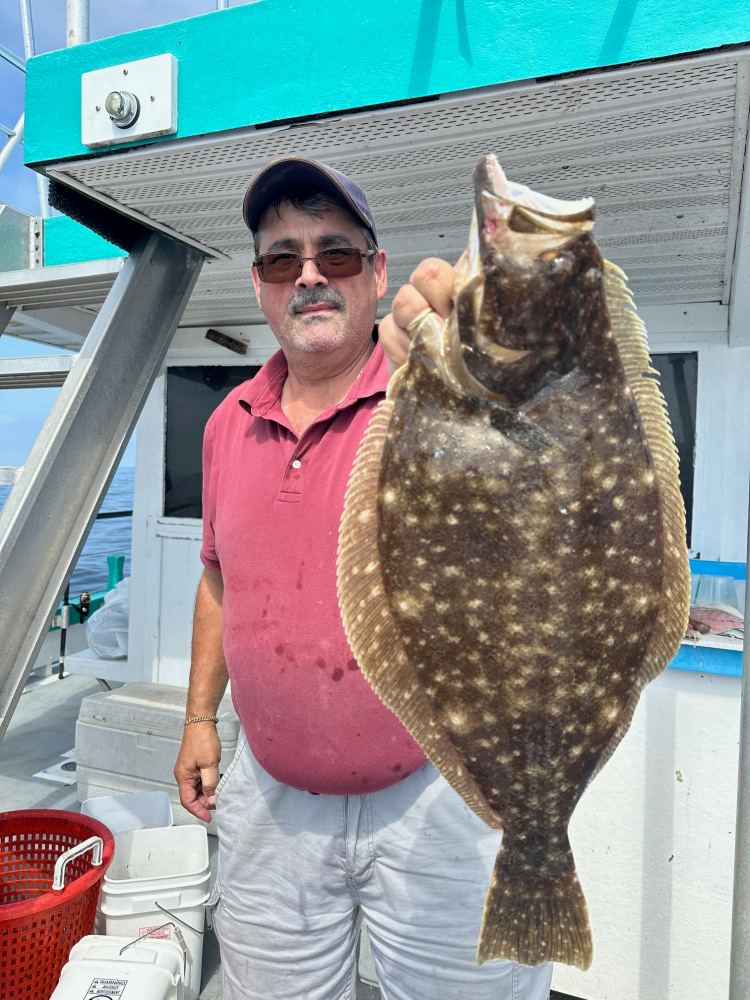 Man in red shirt holding a large flatfish on a boat deck.