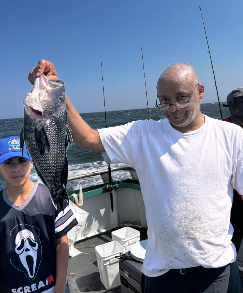 Man holding a large fish on a boat, with a young person beside him.