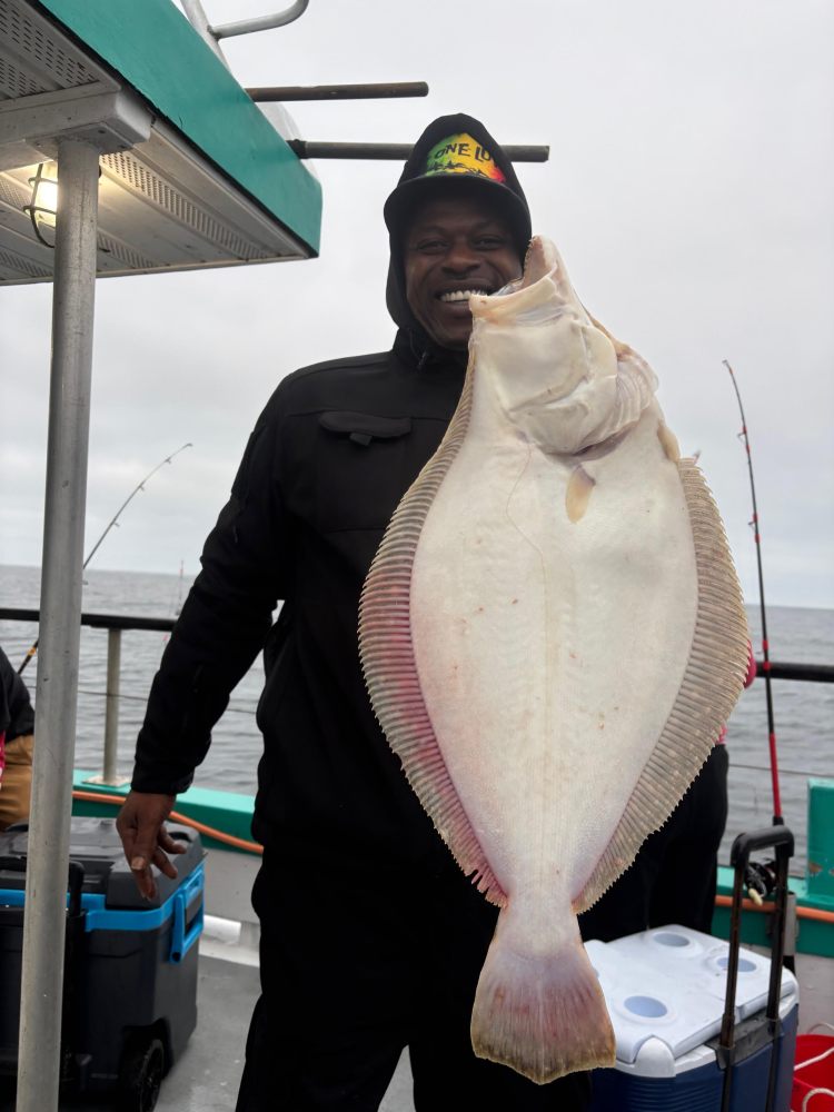 Person on a boat holds a large flat fish, smiling on a cloudy day.