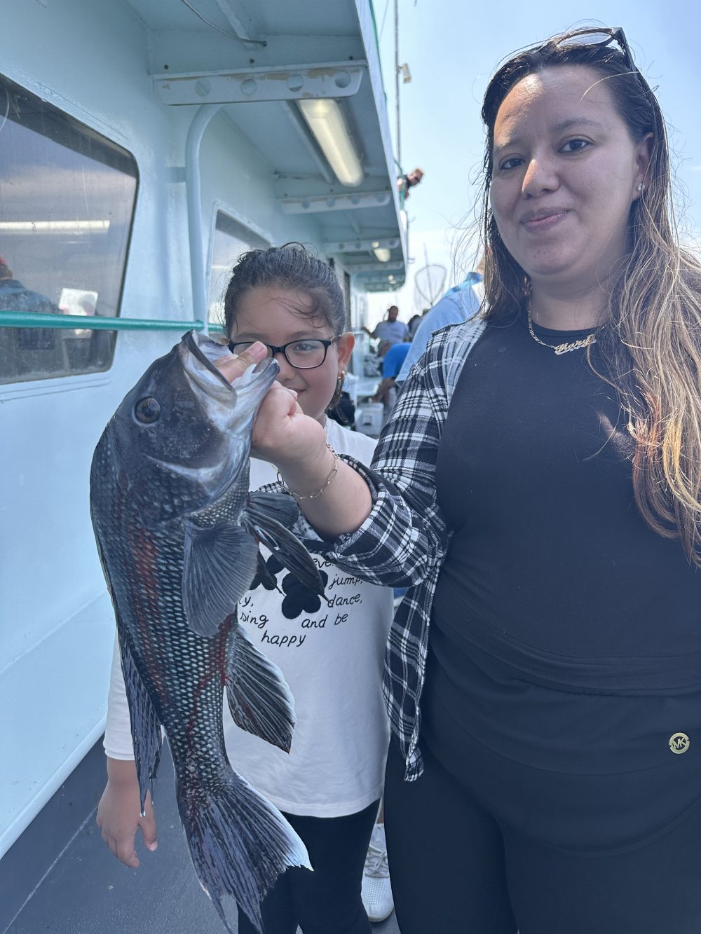 Woman and child holding a large fish on a boat with other people in the background.