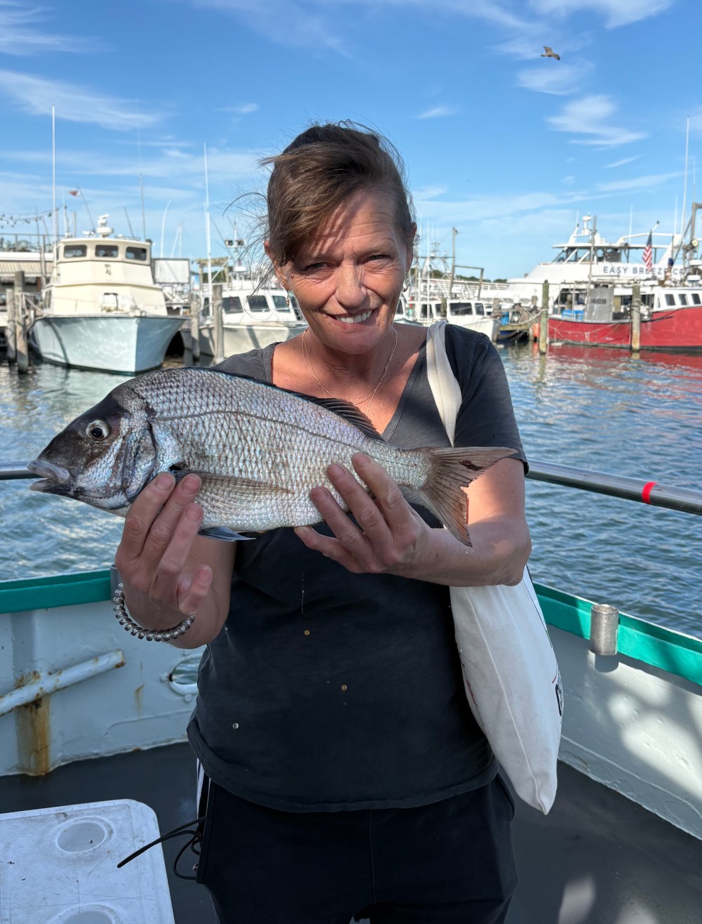 Person holding a fish with boats in the background on a sunny day.
