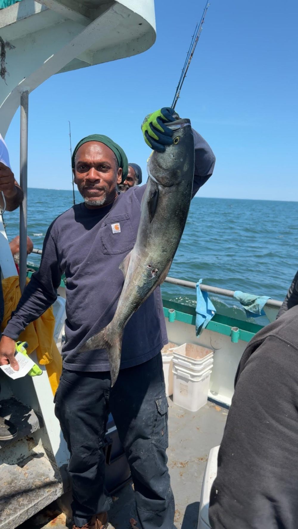 Man on a boat holding a large fish with ocean in the background.