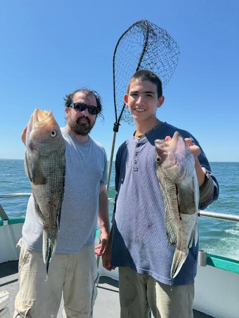 Two people on a boat holding freshly caught fish with a fishing net behind them.