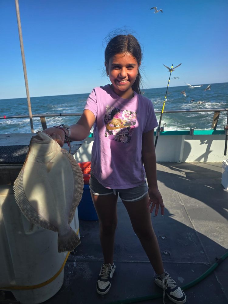 Girl holding a fish on a boat with ocean and seagulls in the background.