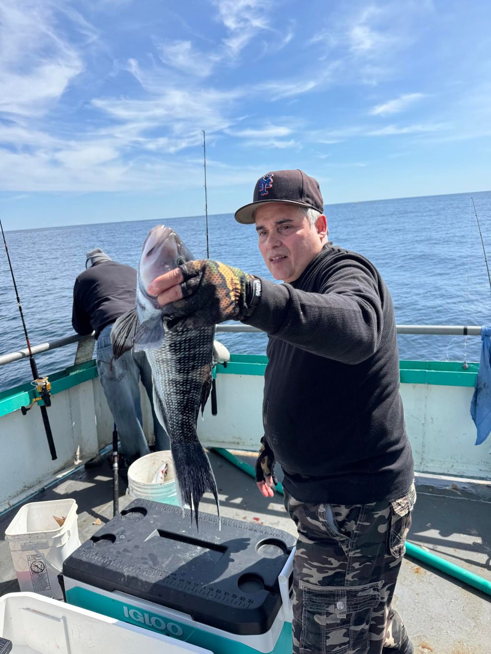 Person on a boat holding a fish with ocean and blue sky in the background.