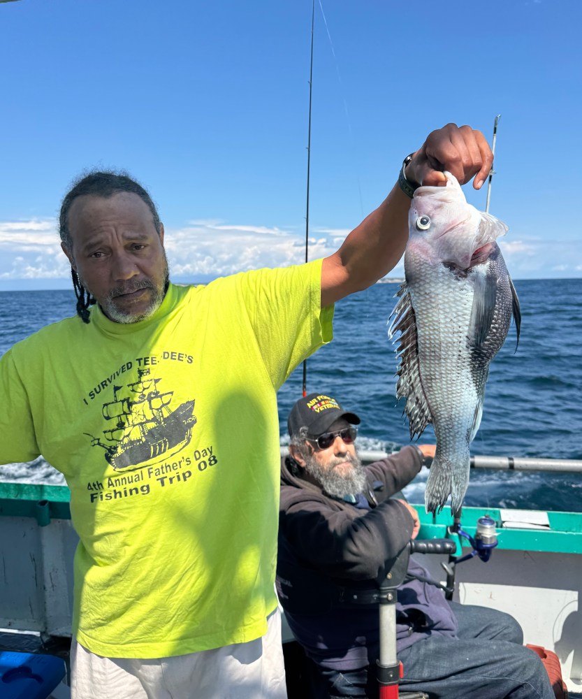 Man in yellow shirt holding fish on a boat with another person sitting behind him.