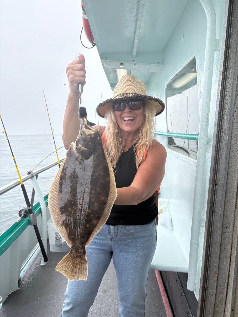 Woman in hat holding a large fish on a boat, smiling.