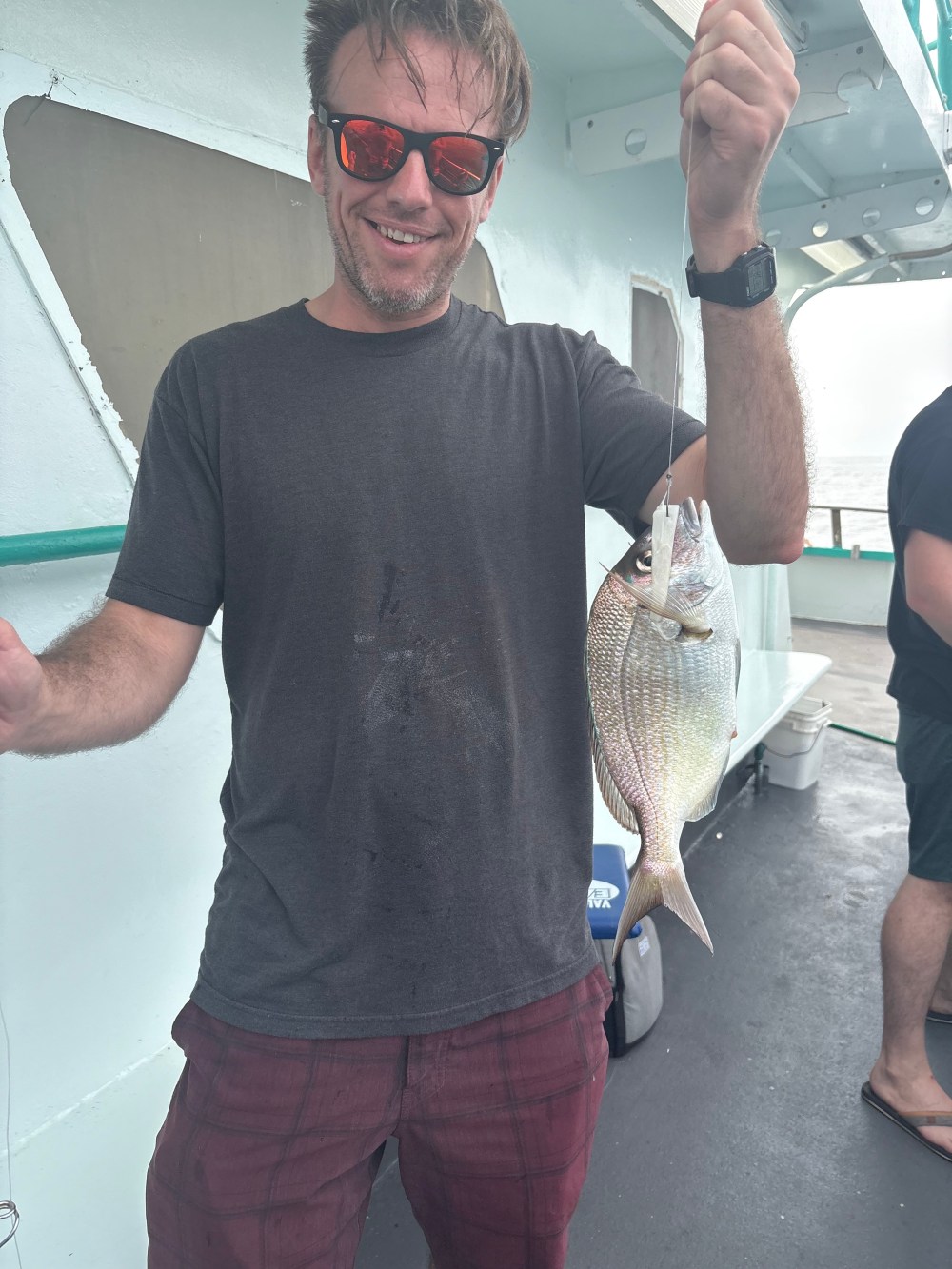 Person wearing sunglasses holding a fish on a boat.