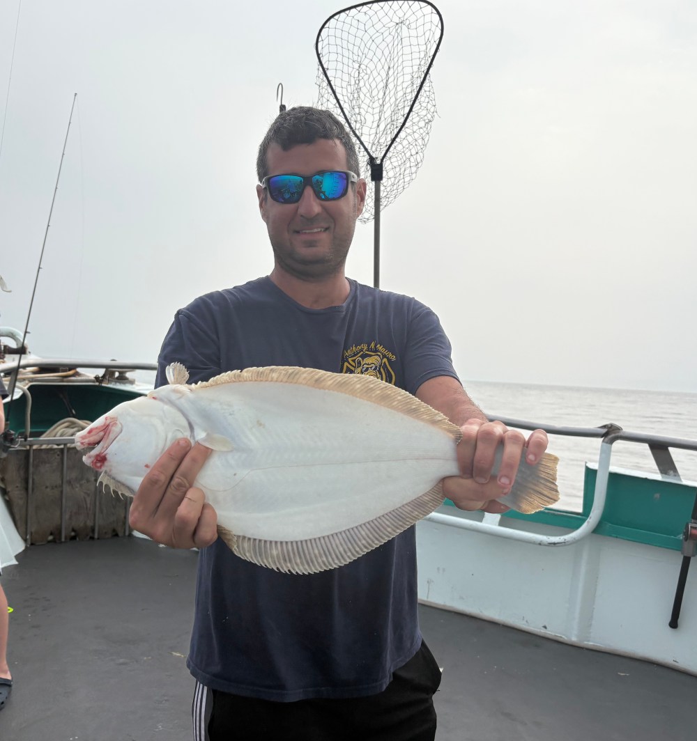 Person on a boat holding a large flat fish, with a fishing net in the background.