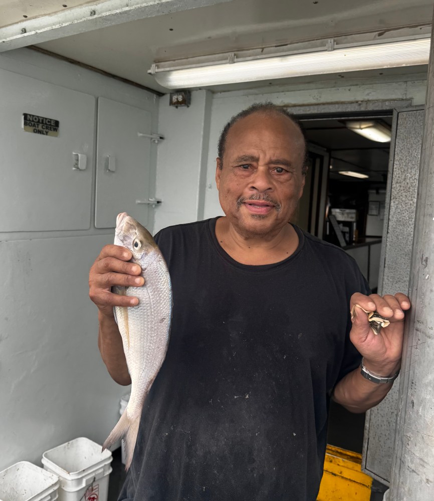 Man in black shirt holding a fish, standing inside a boat cabin.