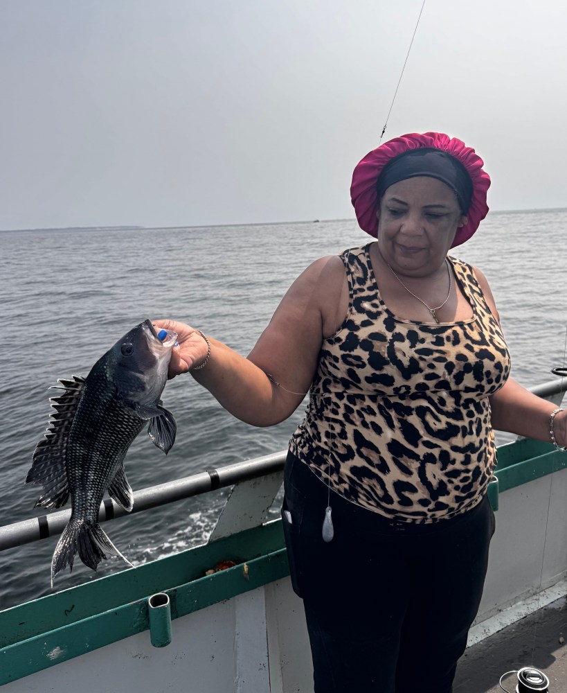 Person holding a fish on a boat, wearing a leopard print top and pink headscarf.