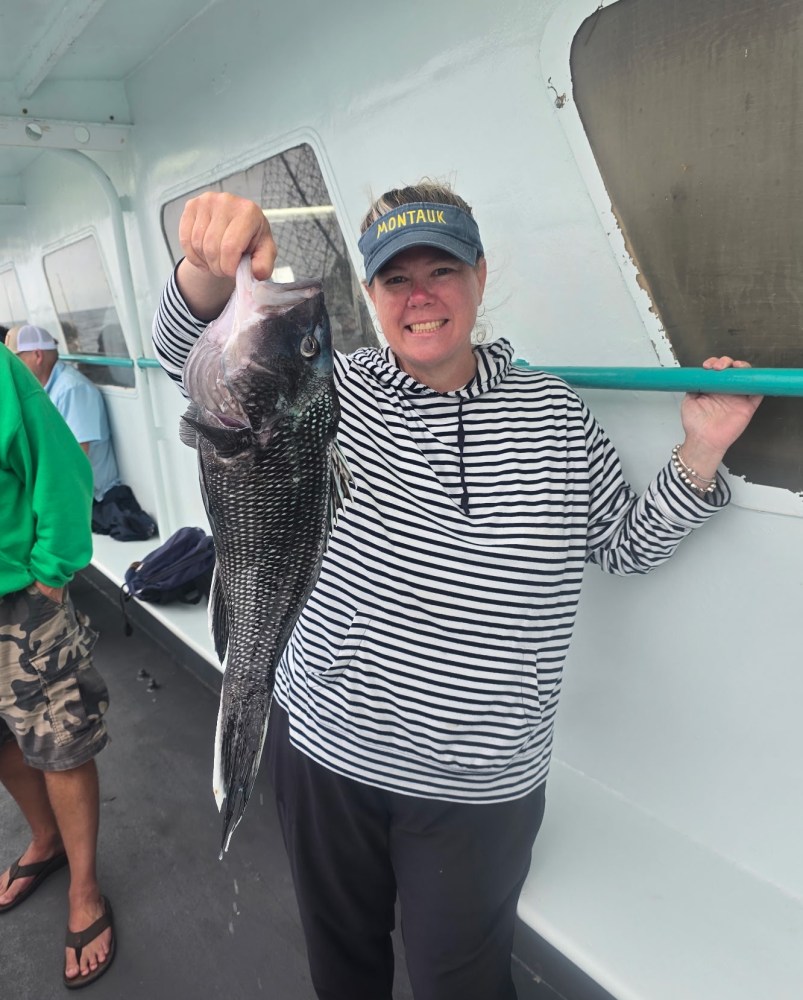 Person in striped shirt holding a large fish on a boat, wearing a Montauk visor.