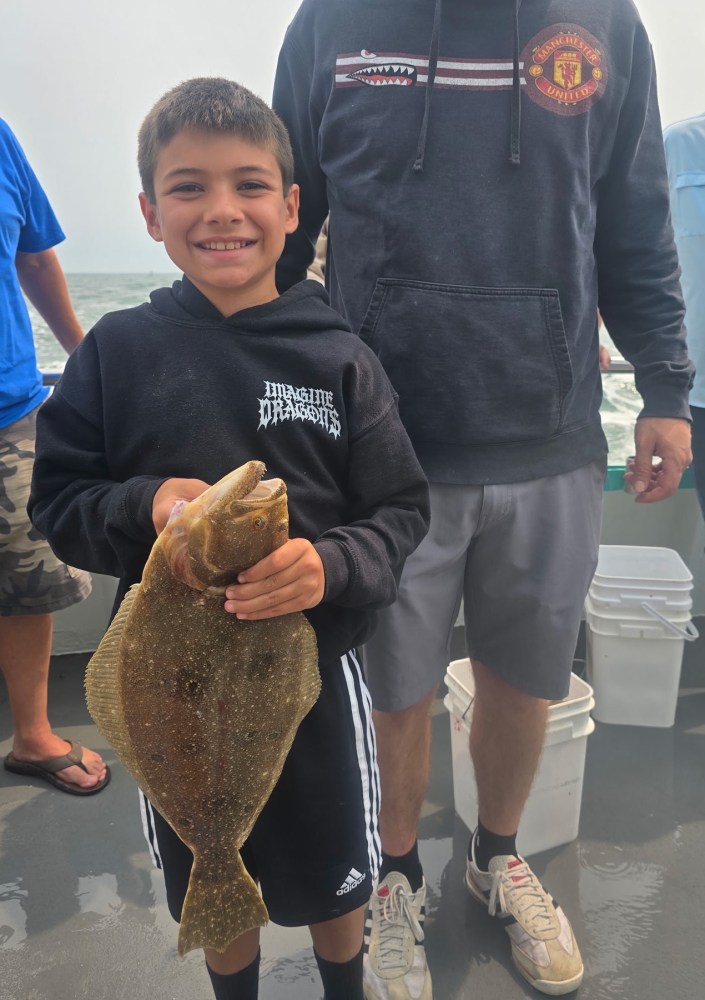 Boy in black hoodie smiling while holding a fish on a boat.