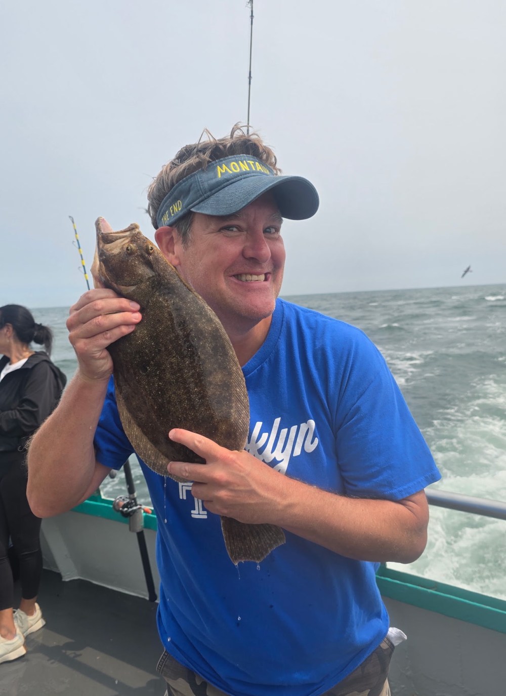Person smiling and holding a fish on a boat with the ocean in the background.