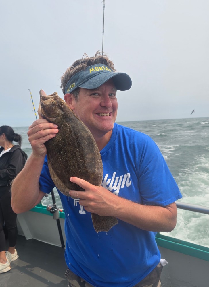 Person on boat holding a fish up to their cheek, smiling with ocean in background.