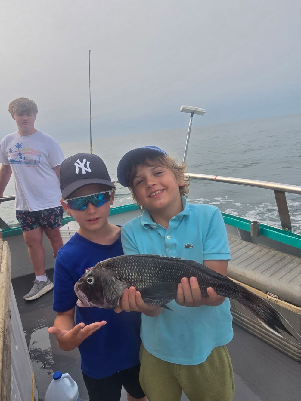 Two kids on a boat holding a large fish, with another person in the background.
