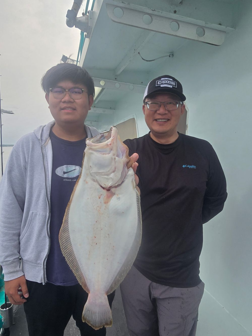 Two people on a boat holding a large flat fish together, both smiling.