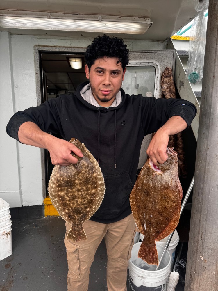Person holding two flatfish on a boat in casual attire.